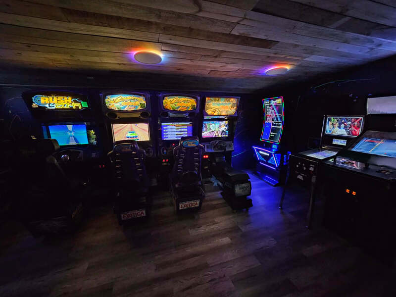 Racing and pinball arcade cabinets lit up in the Highland Hideaways arcade